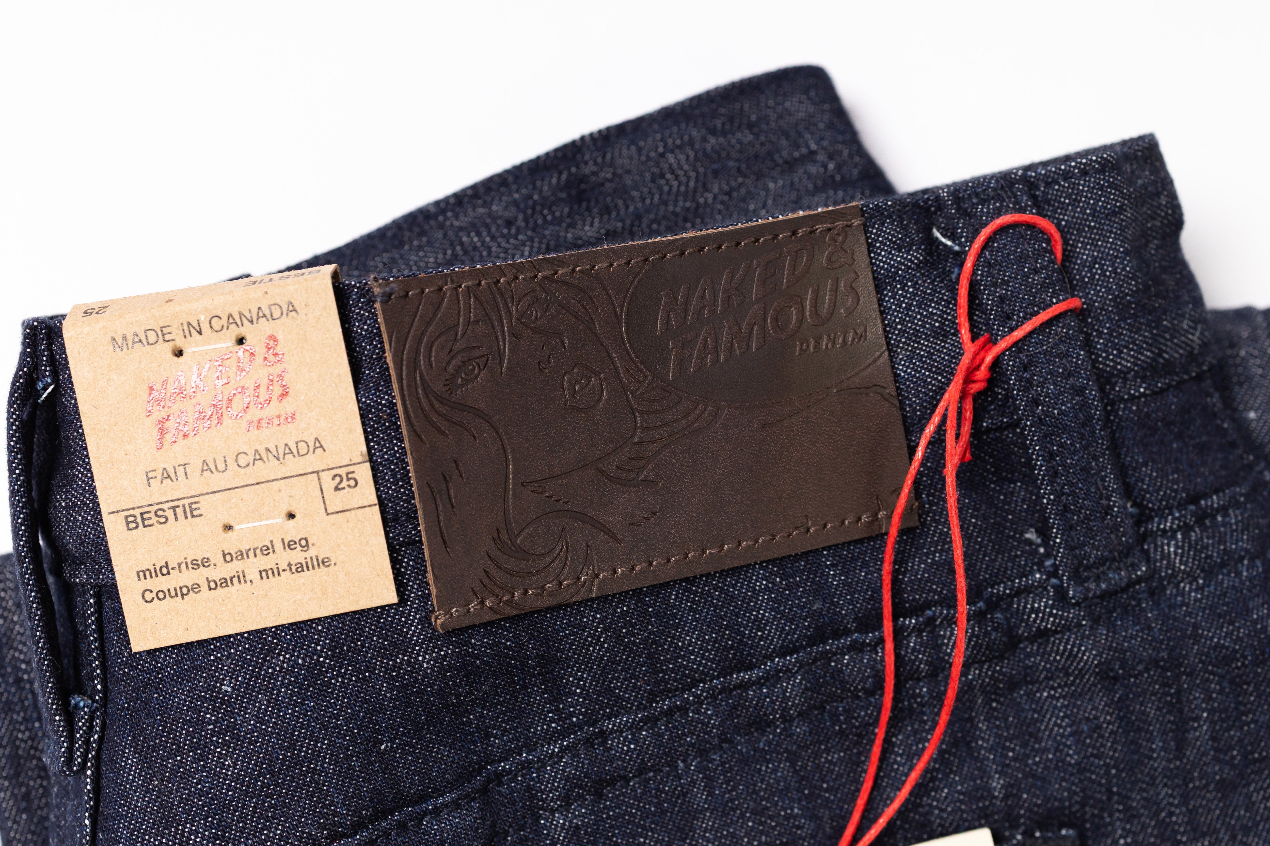 Close-up of dark blue jeans with a brand label and tag on a white background
