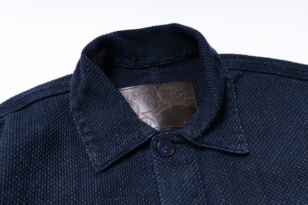 Close-up of a navy blue textured shirt collar with a button on a white background