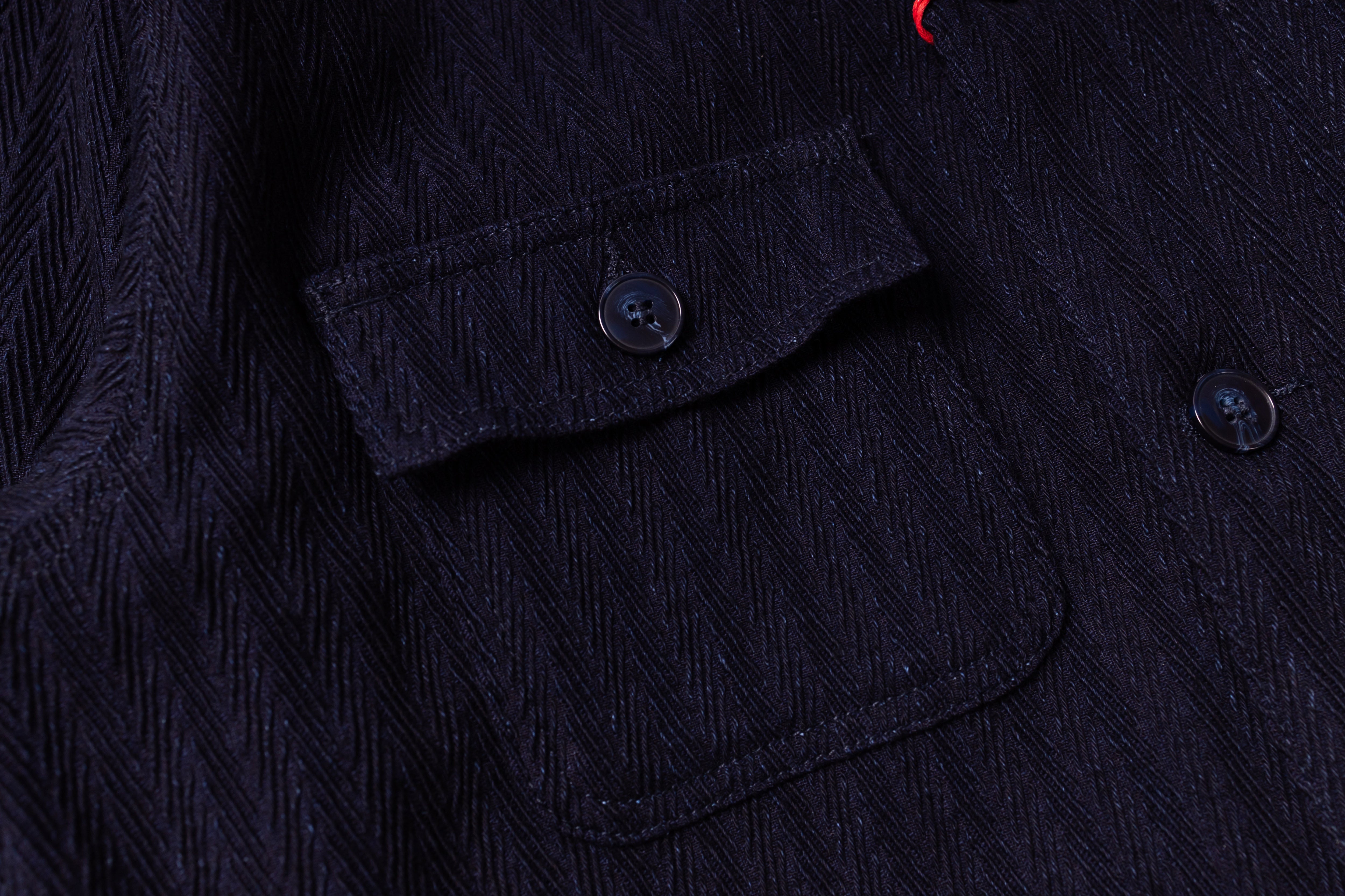 Close-up of a dark textured fabric with buttons and a pocket