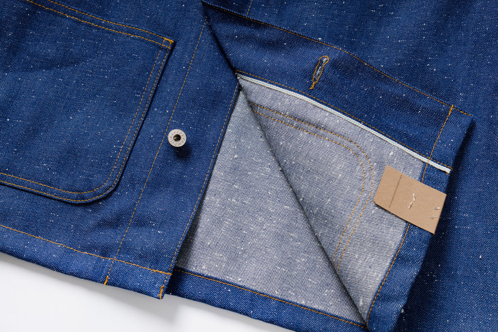 Close-up of a blue denim jacket with a button and label on a white background