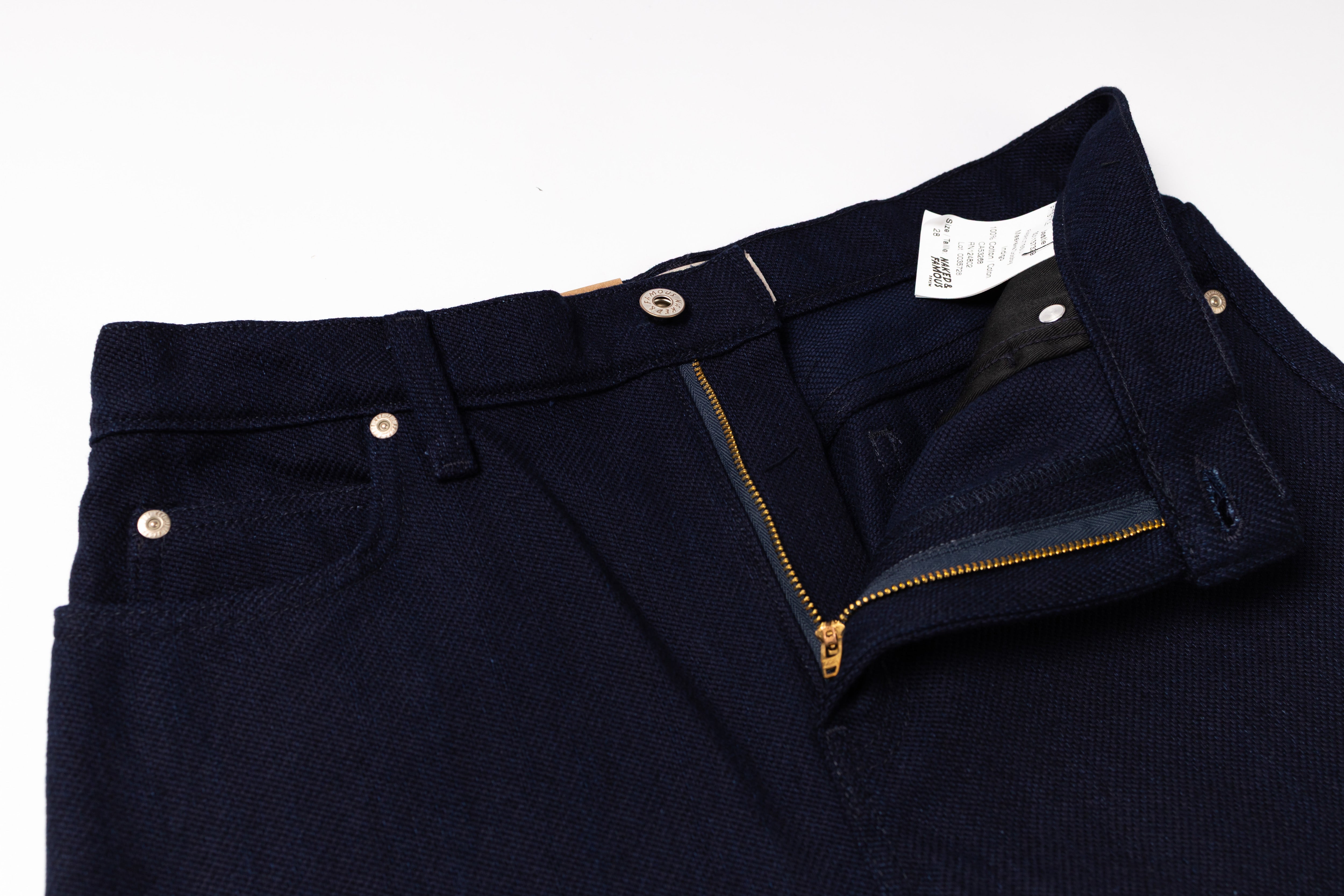 Close-up of a pair of dark navy blue jeans showing the waistband, belt loops, front pocket, and open zipper fly on a white background.