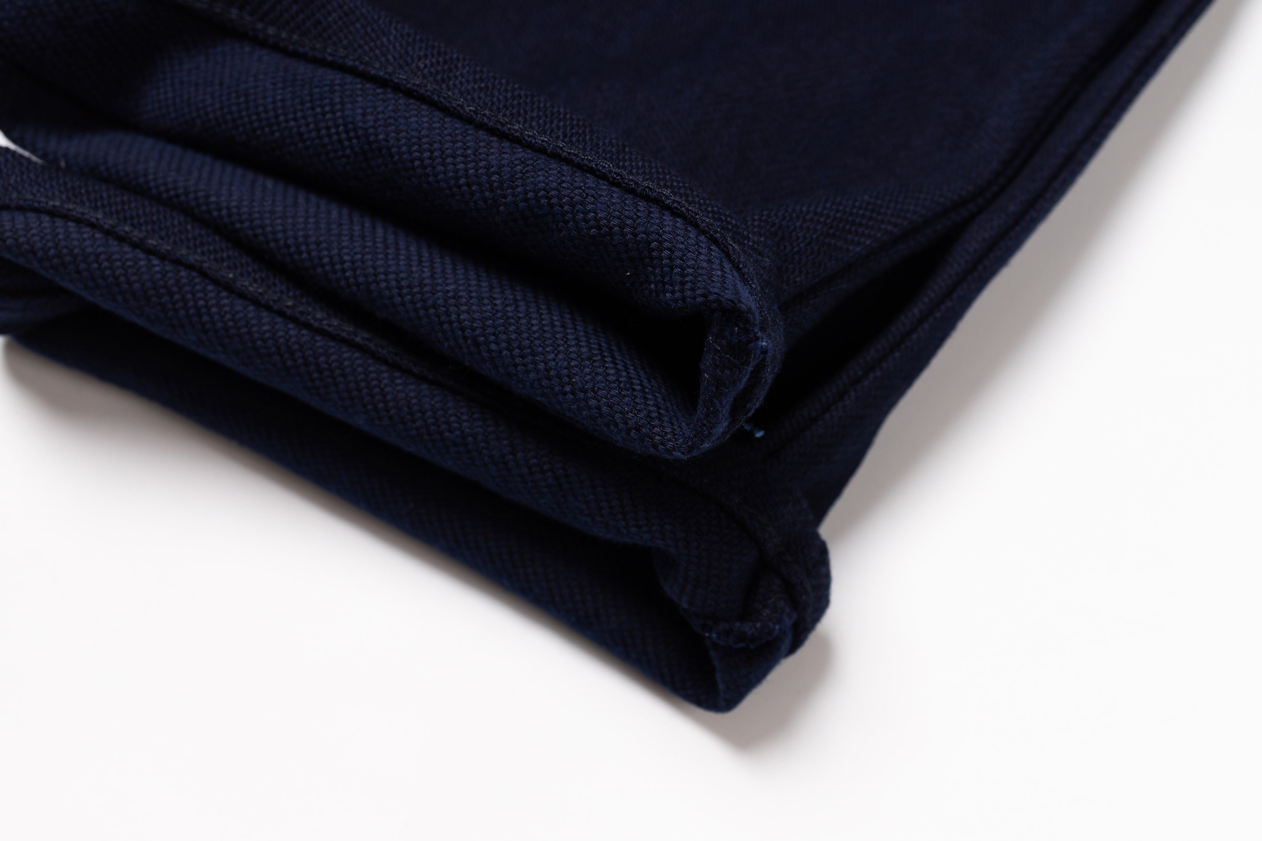 A close-up of folded dark navy blue fabric, showing the woven texture and stitched edges, set against a plain white background.