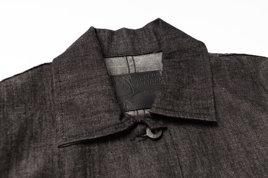 Close-up of a dark gray coat with a collar and brand label on a white background