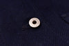 A close-up of a silver metal snap button with the brand name printed on int, set against a dark navy blue textured fabric background.