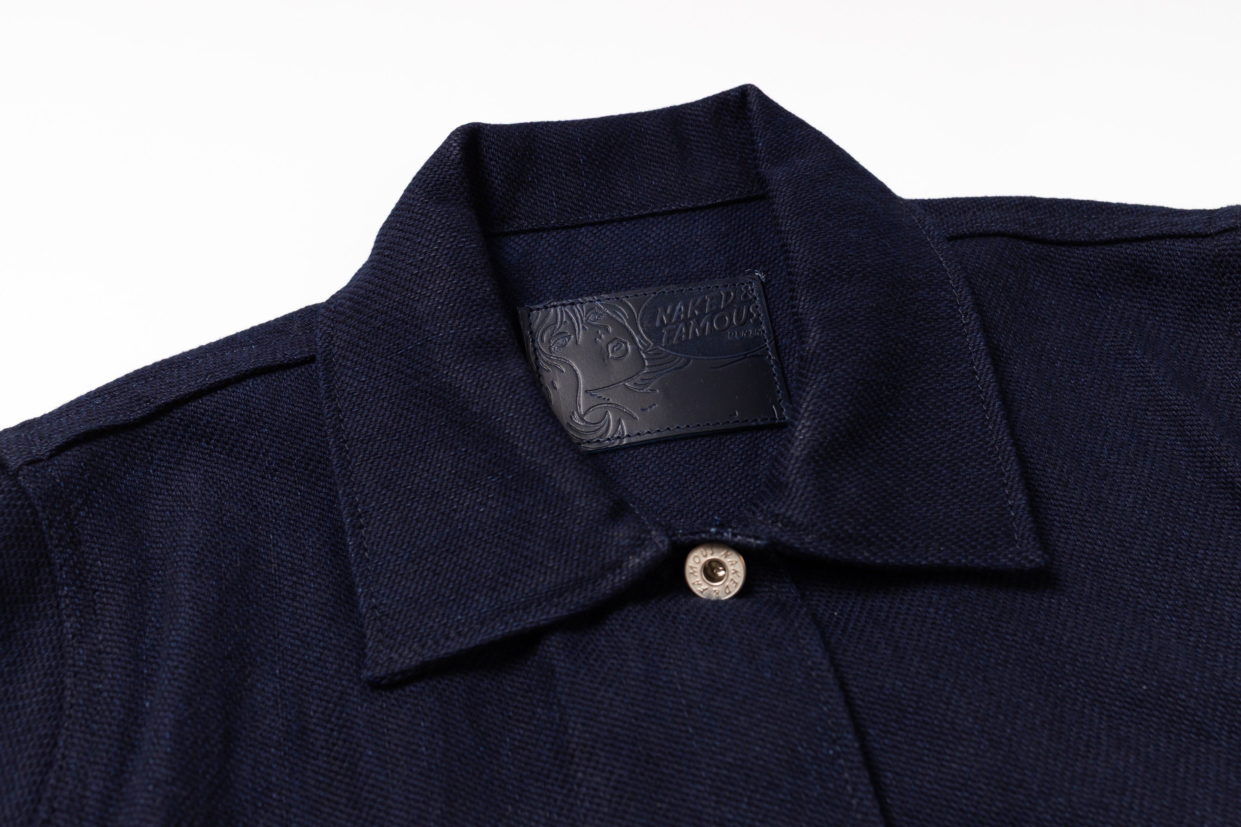 Close-up of a dark navy blue textured knit polo shirt collar with a single silver button and a black brand label inside the neck.