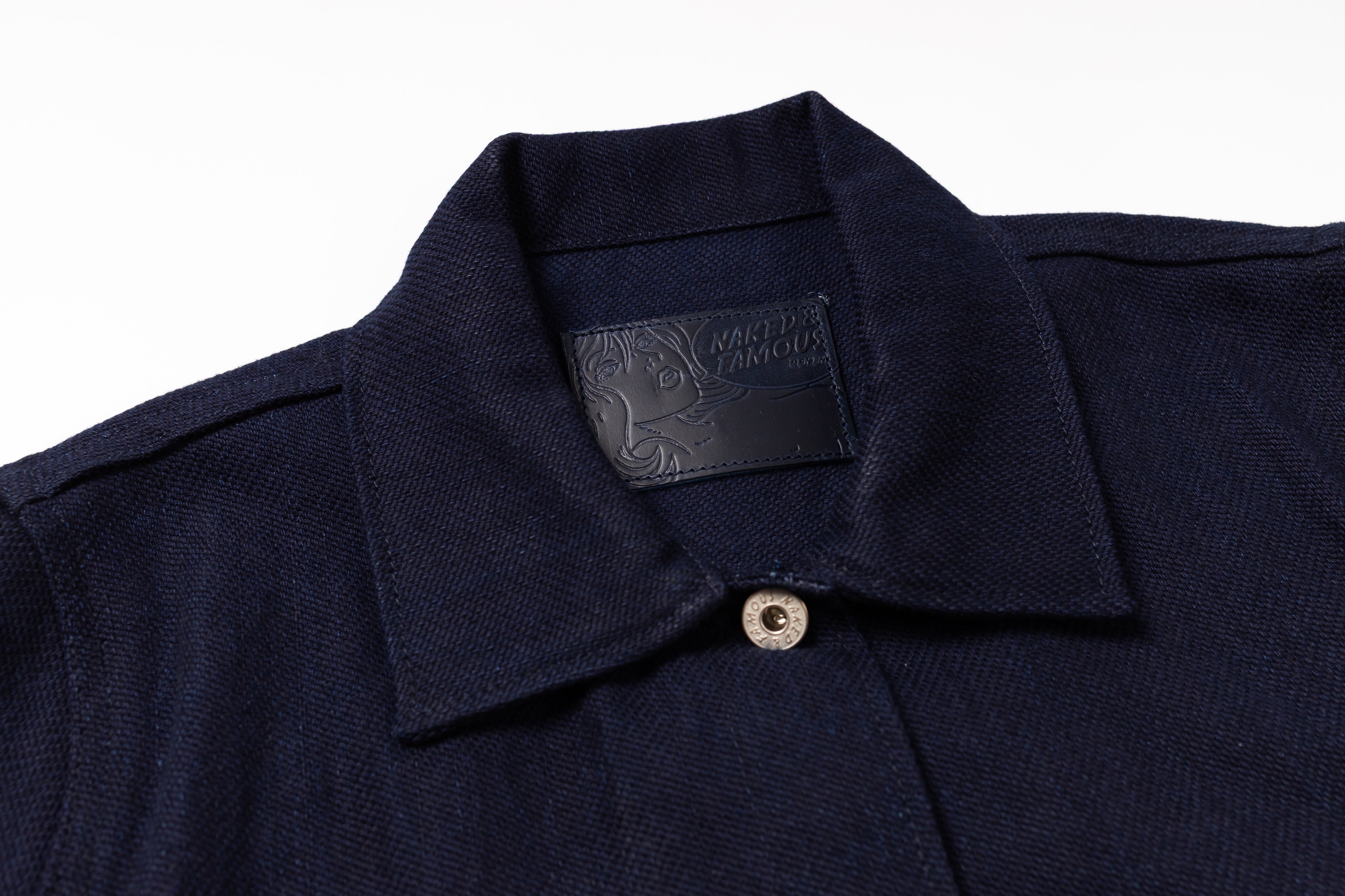 Close-up of a dark navy blue textured knit polo shirt collar with a single silver button and a black brand label inside the neck.