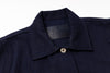 Close-up of a dark navy blue textured knit polo shirt collar with a single silver button and a black brand label inside the neck.