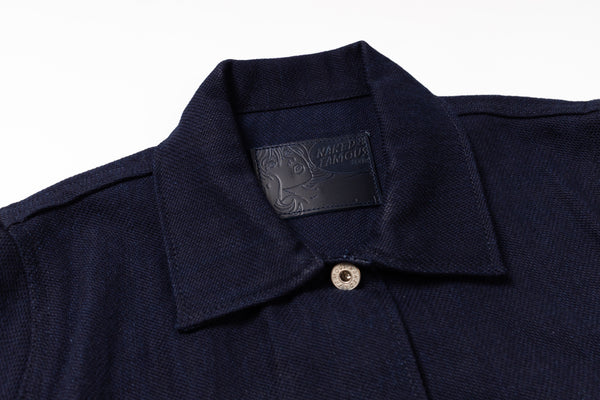 Close-up of a dark navy blue textured knit polo shirt collar with a single silver button and a black brand label inside the neck.