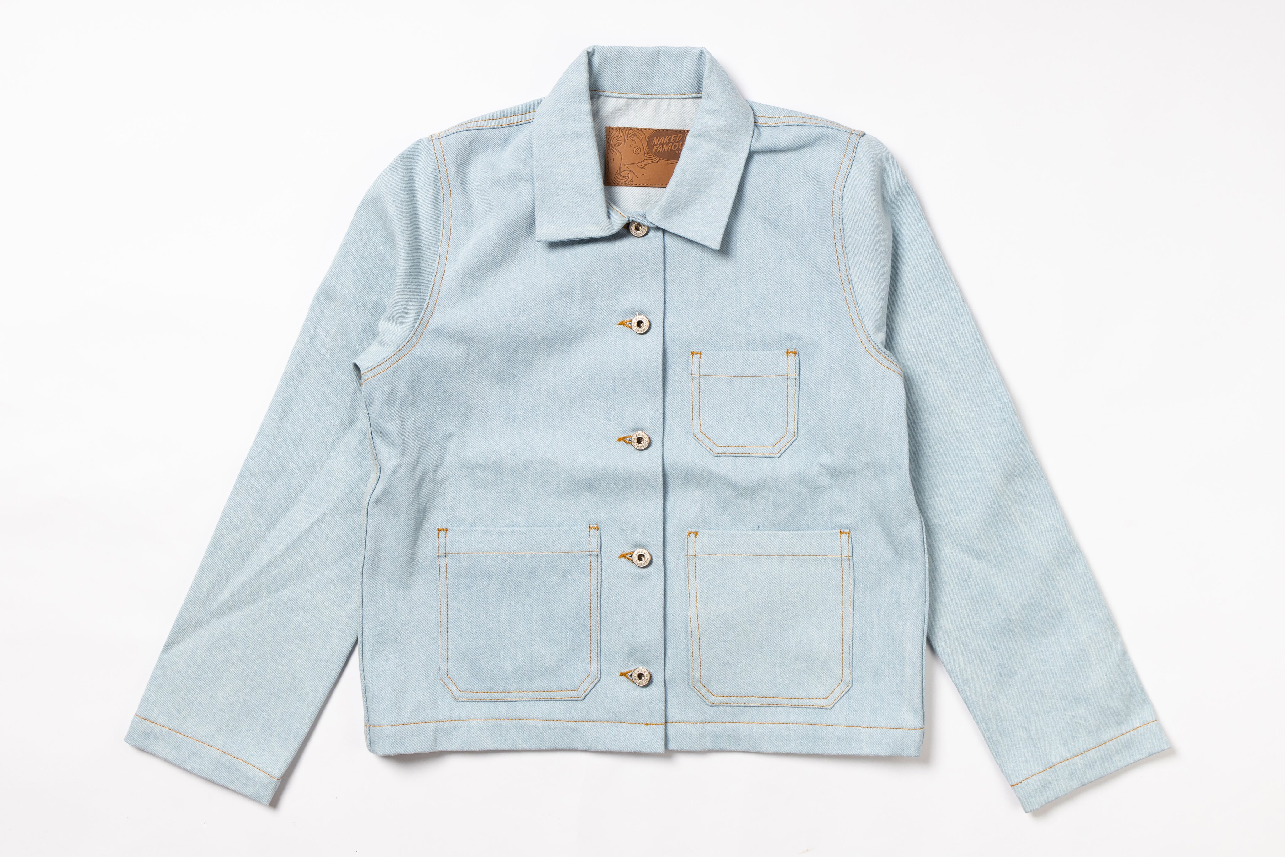A light blue denim work jacket with a pointed collar, button closure, and four front pockets, laid flat against a white background.