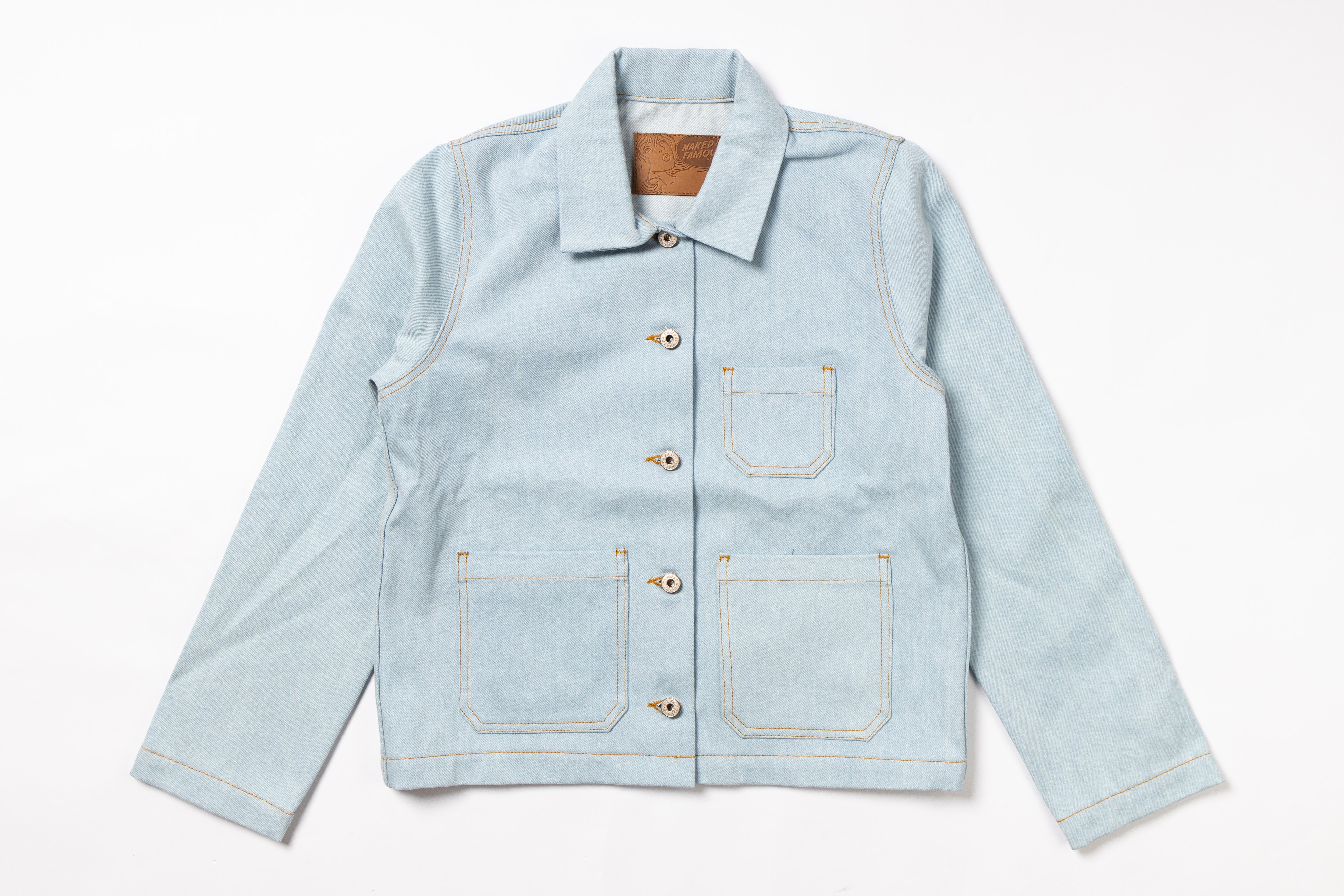 A light blue denim work jacket with a pointed collar, button closure, and four front pockets, laid flat against a white background.