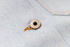 A close-up of a round metallic snap button with the brand name engraved on it, attached to a piece of orange thread, set against a light blue denim fabric background.