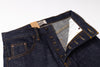 Close-up of a pair of dark indigo denim jeans showing the waistband, button fly, pocket, and interior lining with a paper tag attached.