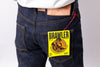Close-up of the back waist of a person wearing dark indigo denim jeans with a yellow Brawler hangtag attached near the pocket, plus a white shirt hem visible at the top.