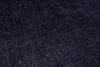 A close-up texture shot of dark indigo denim fabric with visible weave and subtle white flecks.