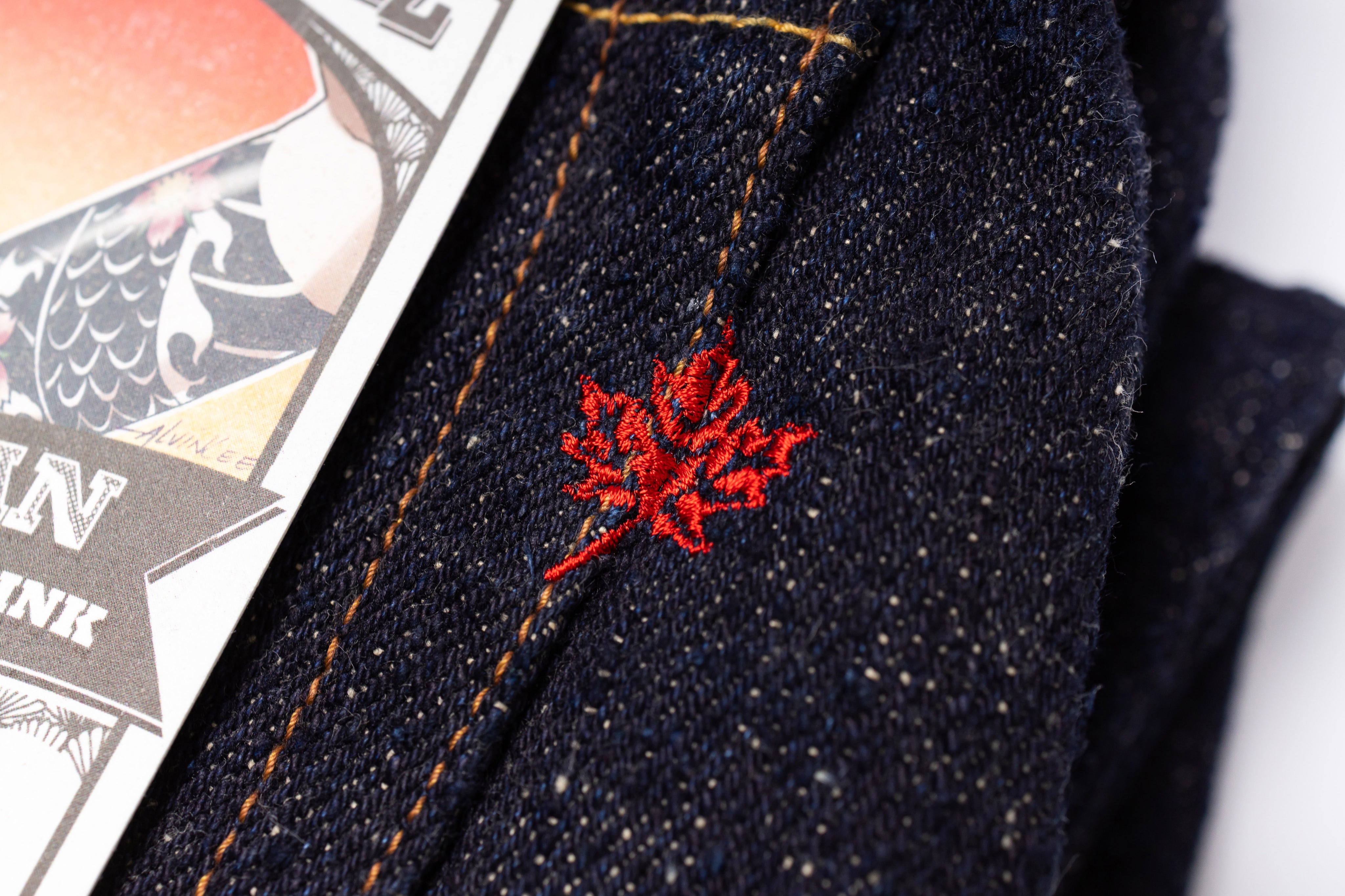 Close-up of dark denim fabric with red floral embroidery, next to a playing card.