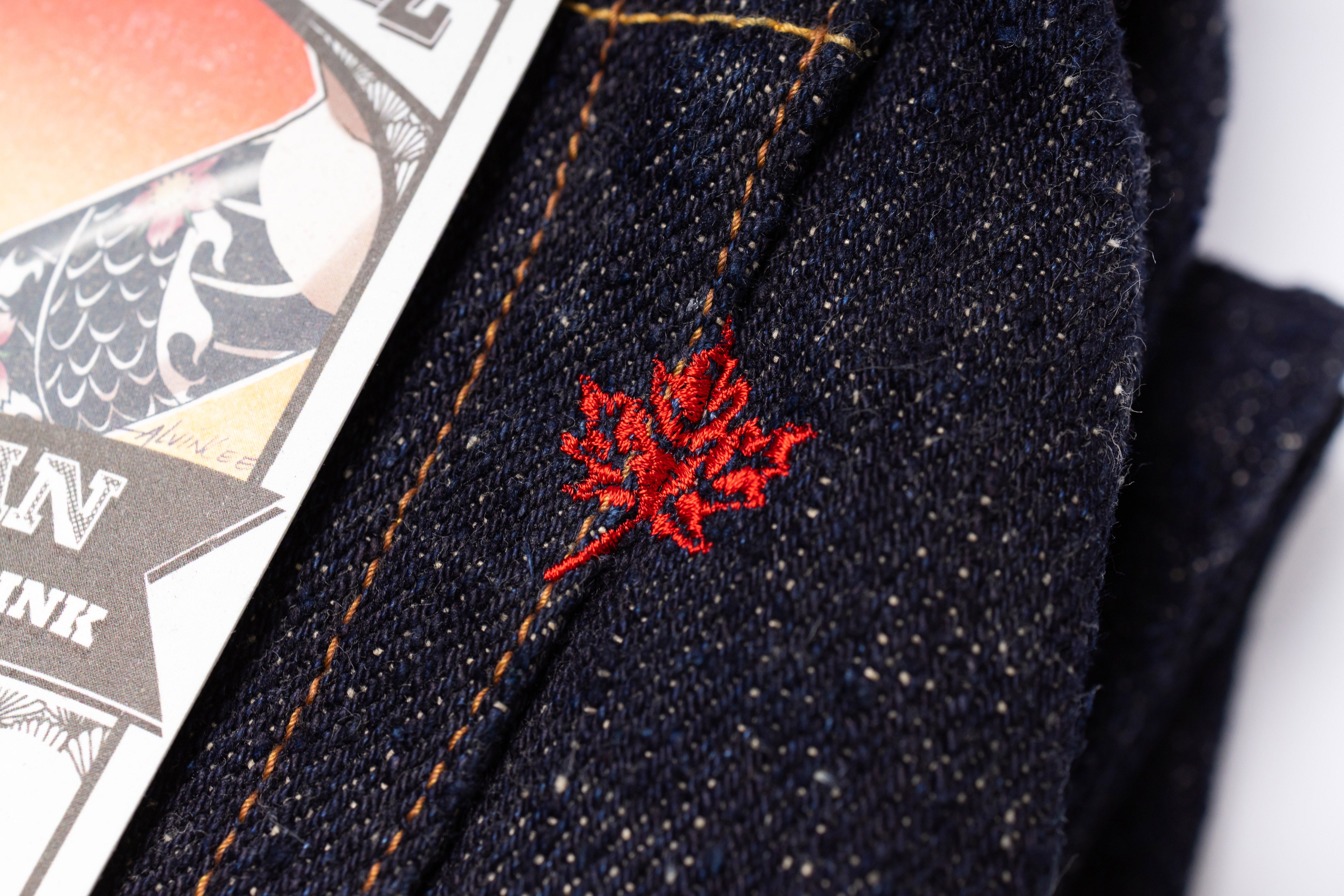Close-up of dark denim fabric with red floral embroidery, next to a playing card.