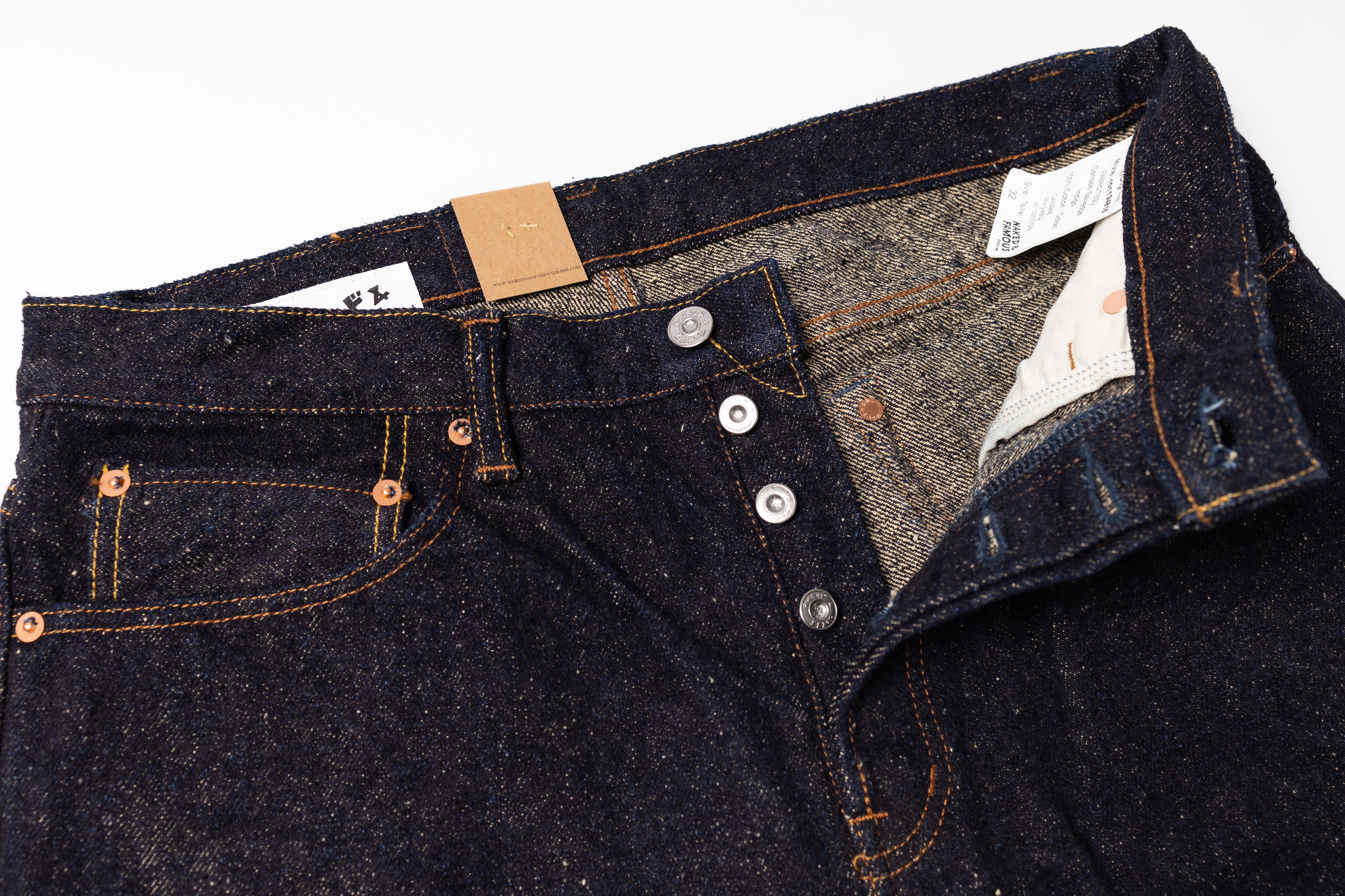 Close-up of a pair of dark blue jeans with buttons and a tag on a white background