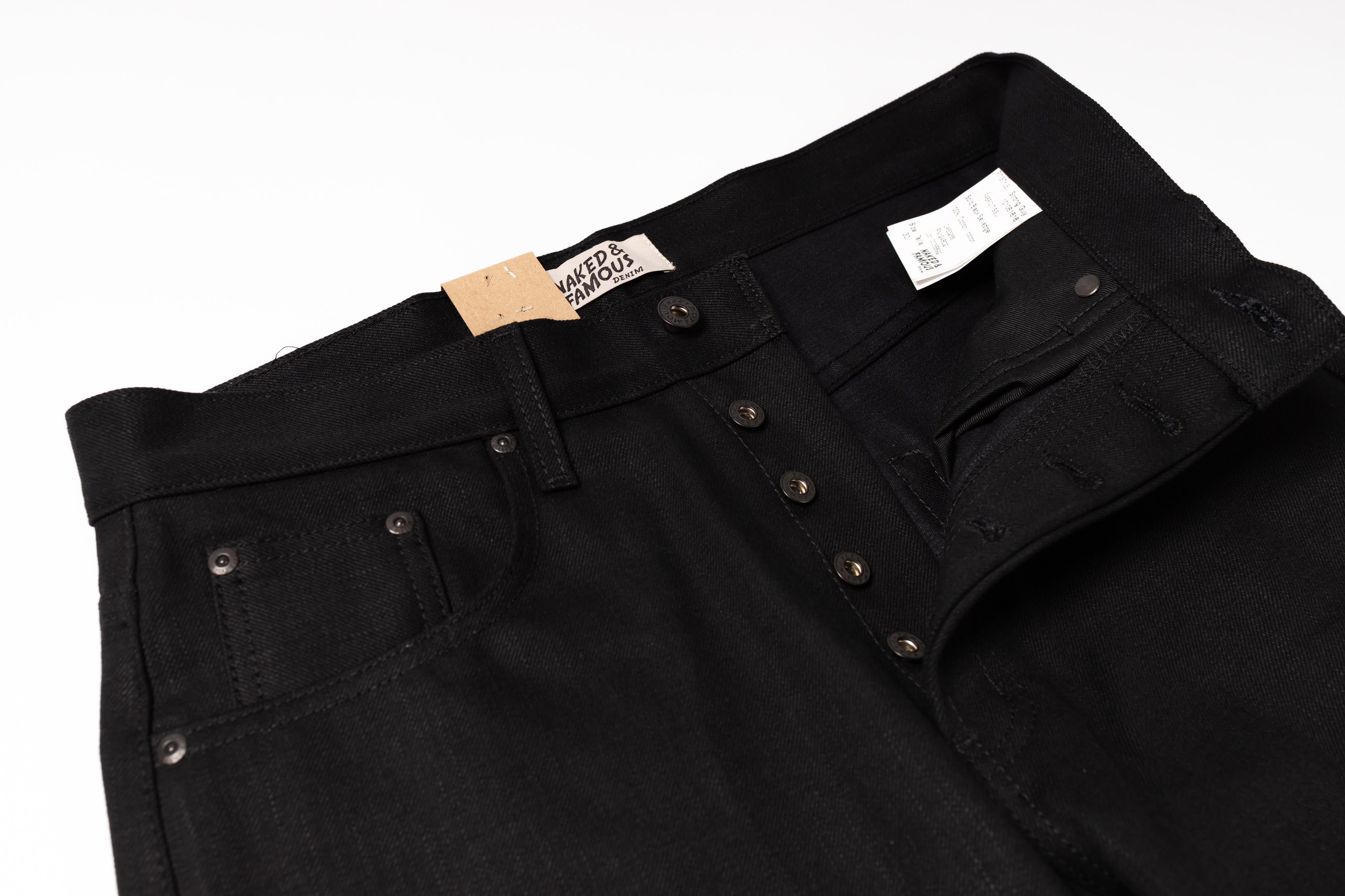 Close-up of black denim jeans showing the waistband, button fly, belt loops, and front pocket on a white background.