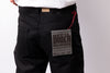 Close-up of a person wearing black denim jeans, showing the back pocket with a paper label that reads 'Solid Black Selvedge' and a red drawstring thread.