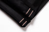 Close-up of a folded black fabric item, likely a garment or textile piece, showing double contrast stitching in a light metallic pink tone along the edge against a white background.