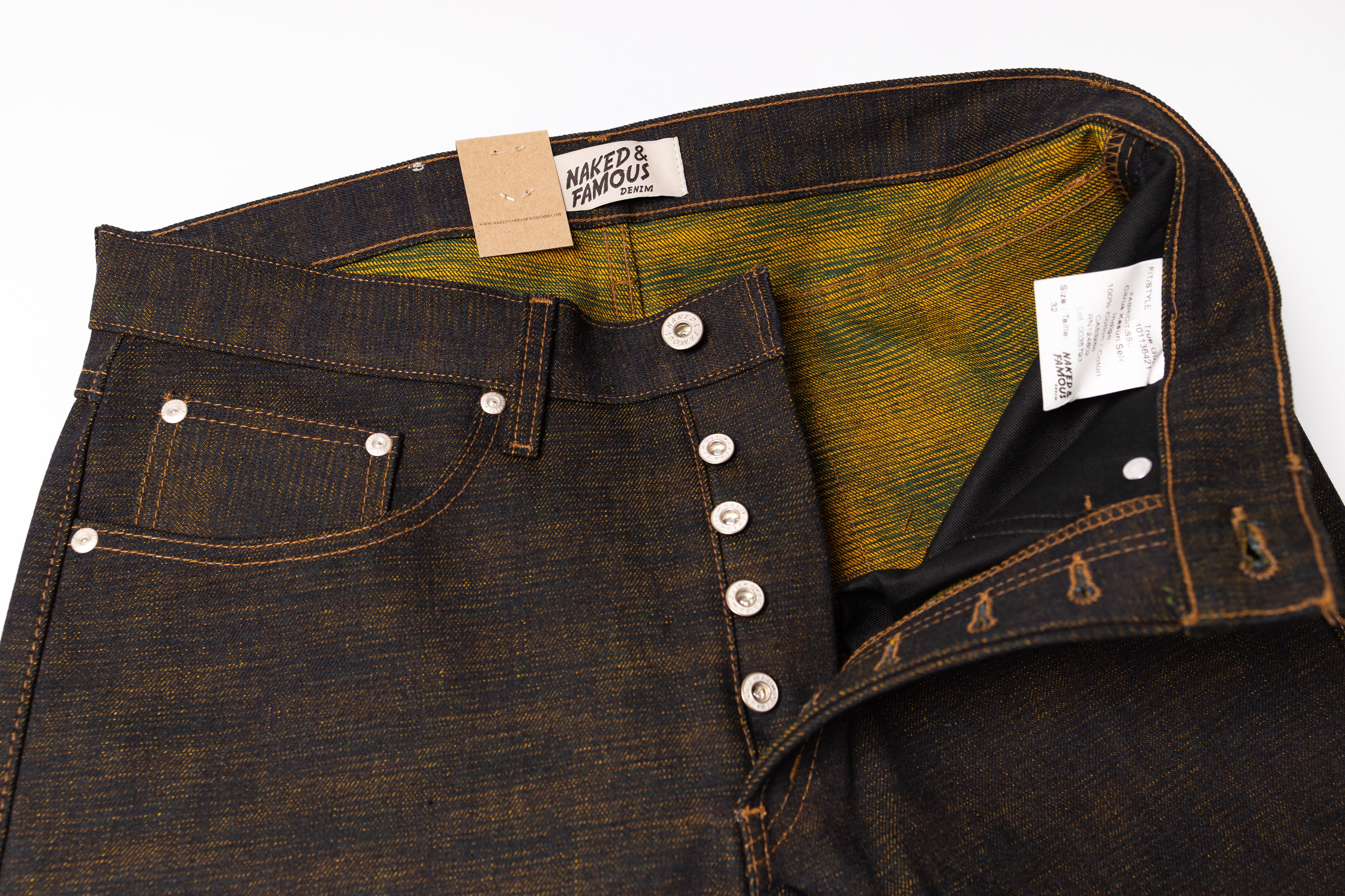 Close-up of dark denim jeans with visible buttons and a brand label on a white background