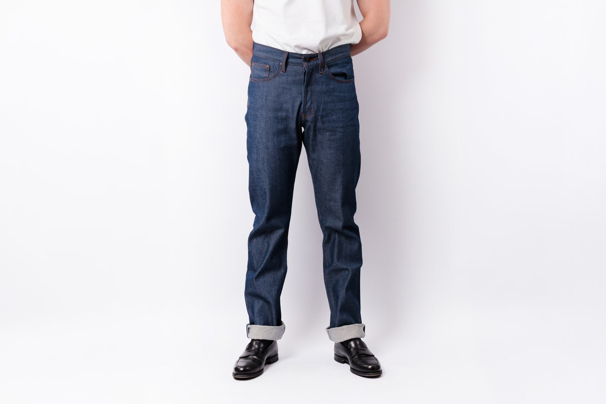 A person wearing dark blue slim-fit jeans, a white shirt, and black leather loafers against a plain white studio background.