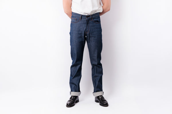 A person wearing dark blue slim-fit jeans, a white shirt, and black leather loafers against a plain white studio background.