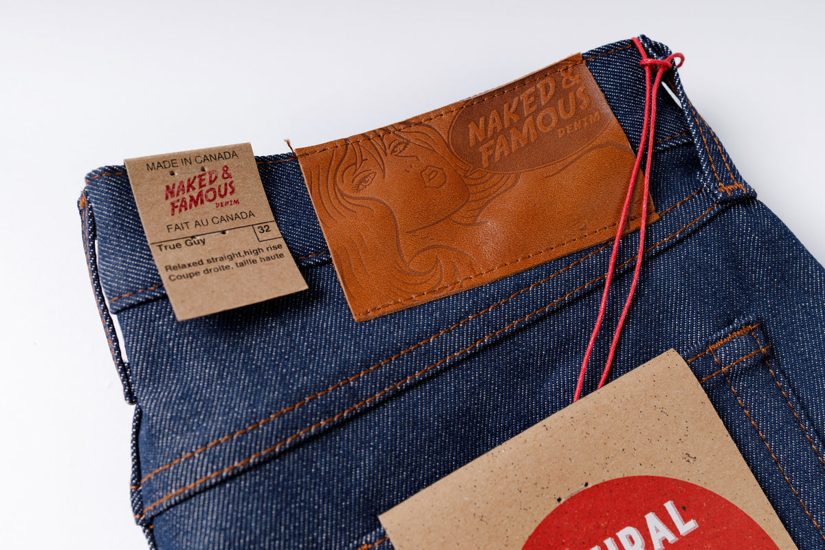 Close-up of blue jeans with 'Naked & Famous' branding on a white background