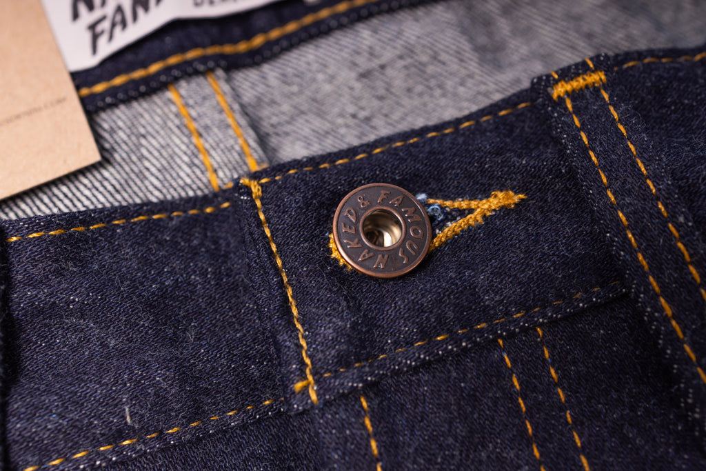 Close-up of a button on a denim jacket with a brand label in the background.