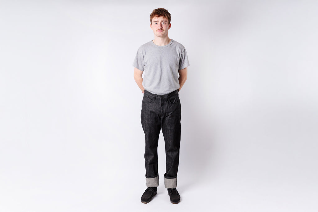 Person wearing a gray t-shirt and dark jeans on a white background