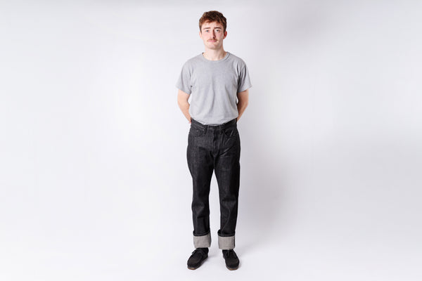 Person wearing a gray t-shirt and dark jeans on a white background