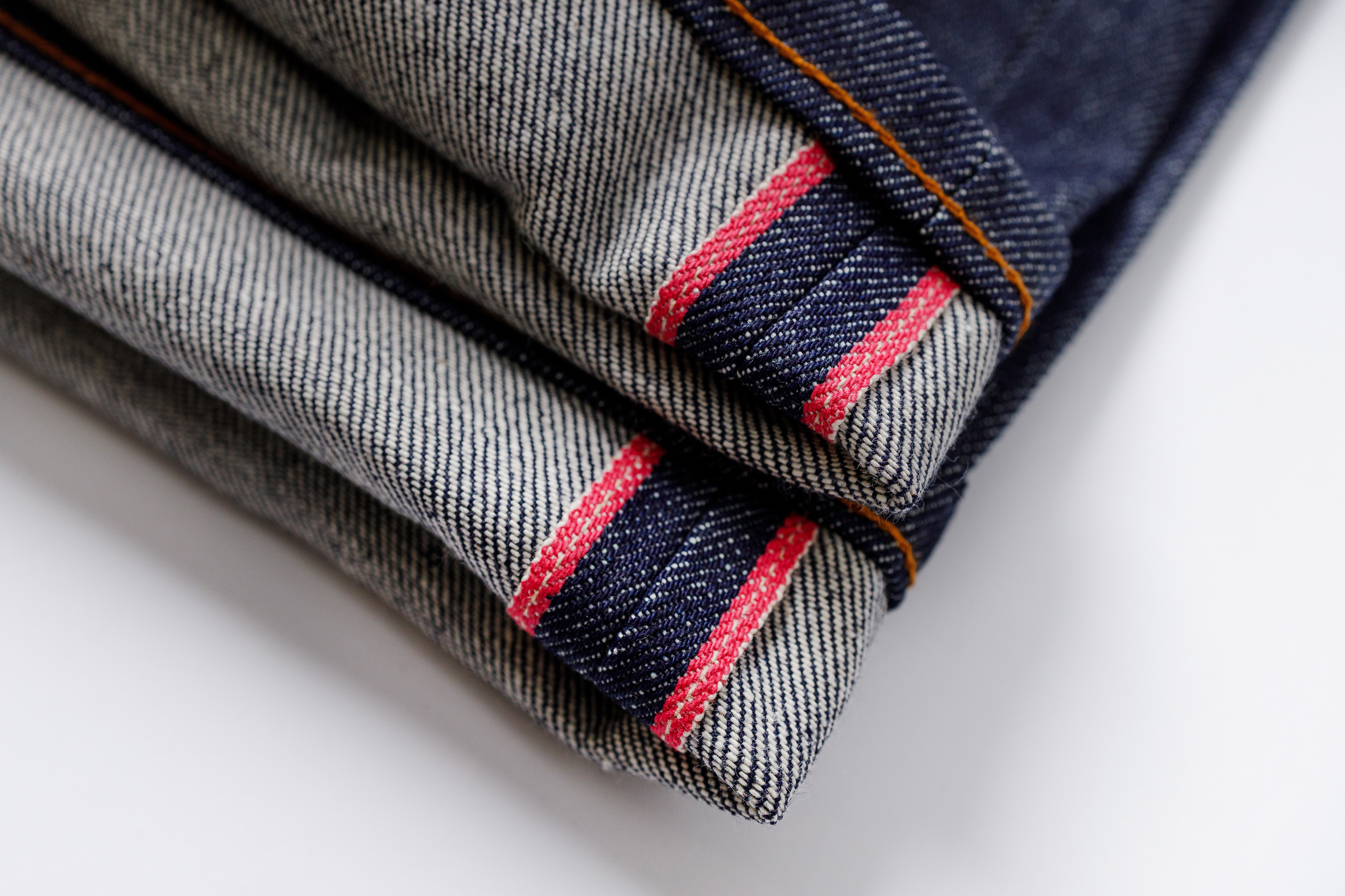 Close-up of folded denim jeans with red stitching on a white background