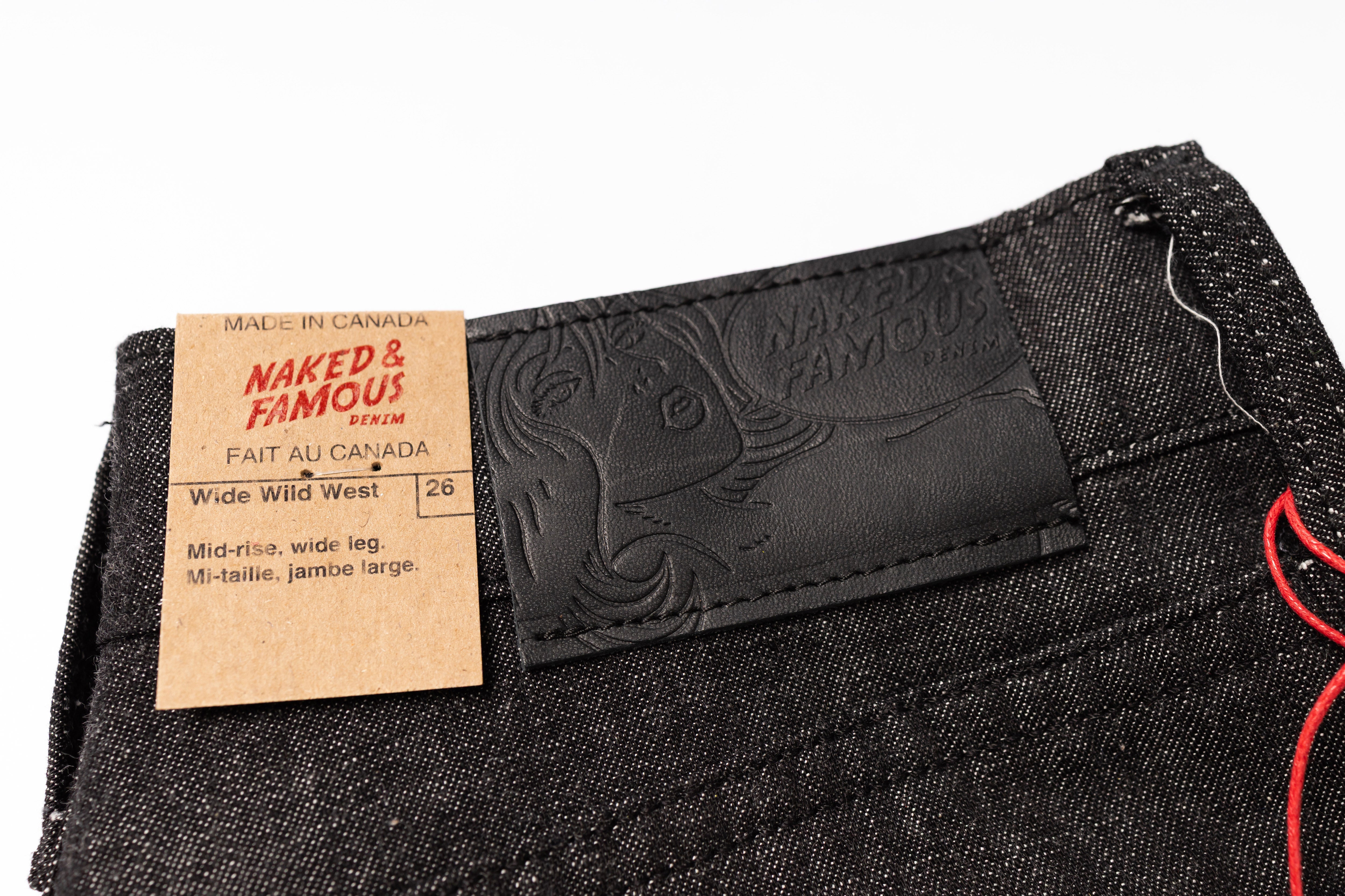 Close-up of black denim jeans with a brand label and tag on a white background