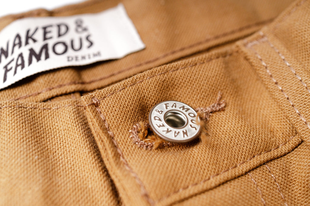 Close-up of a button on brown fabric with 'Naked & Famous' label.