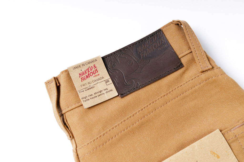 Close-up of a tan pants waistband with a brand label on a white background