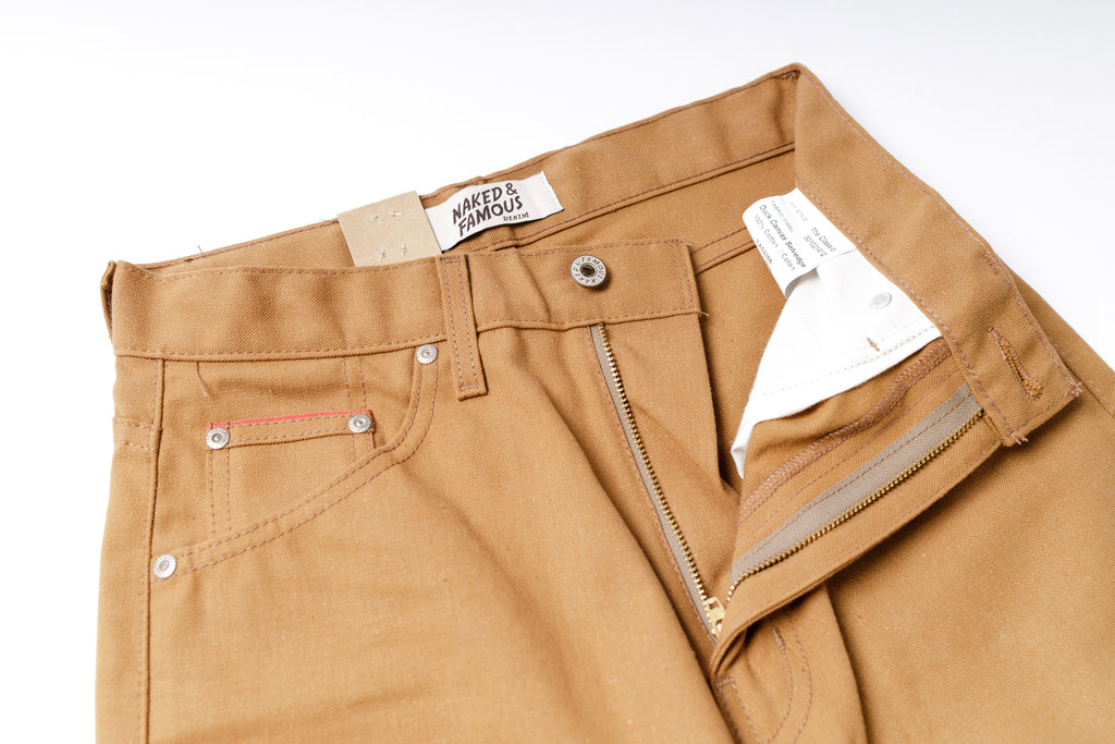 Close-up of tan pants with a brand label on a white background
