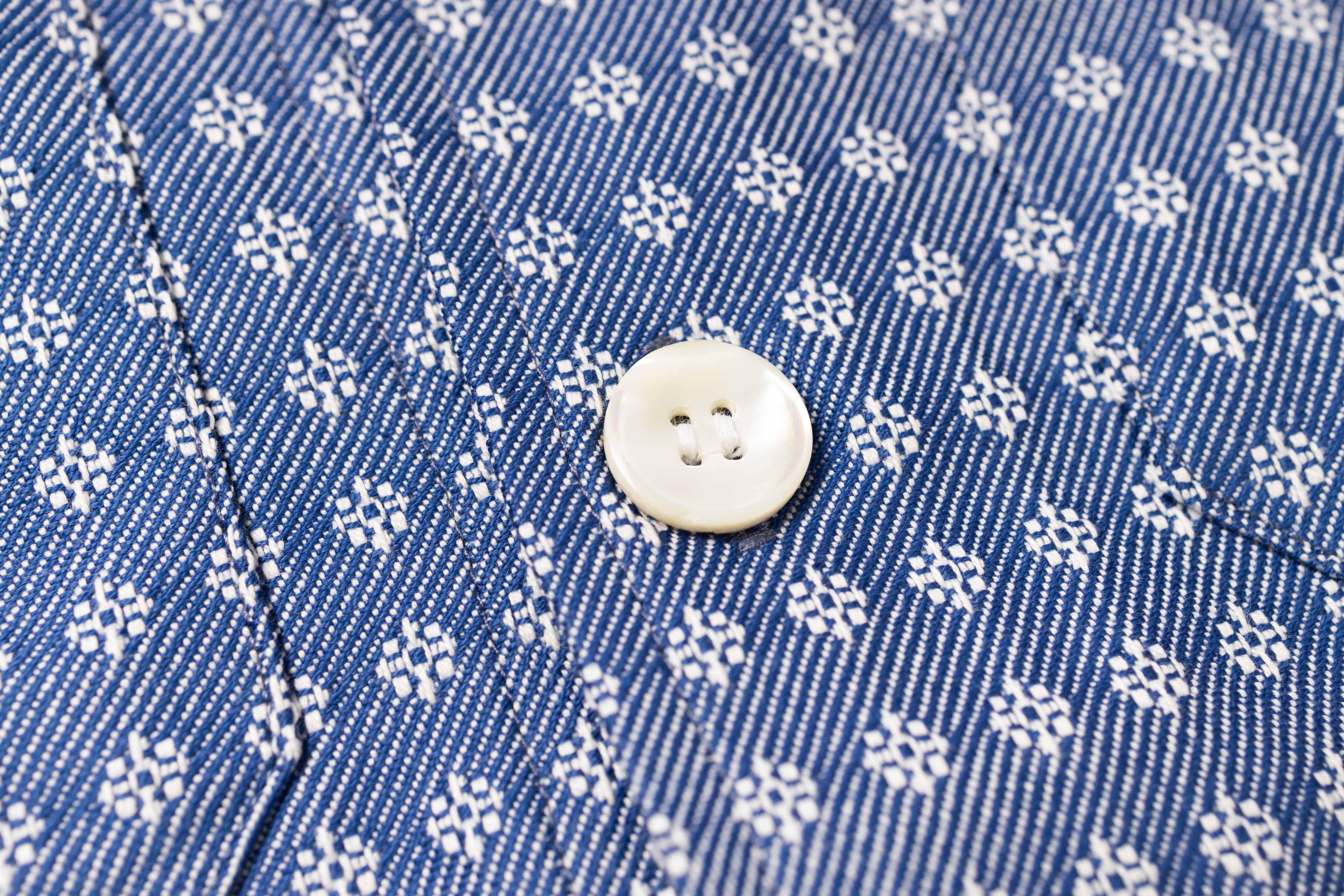 Close-up of a blue denim fabric with white floral pattern and a button.