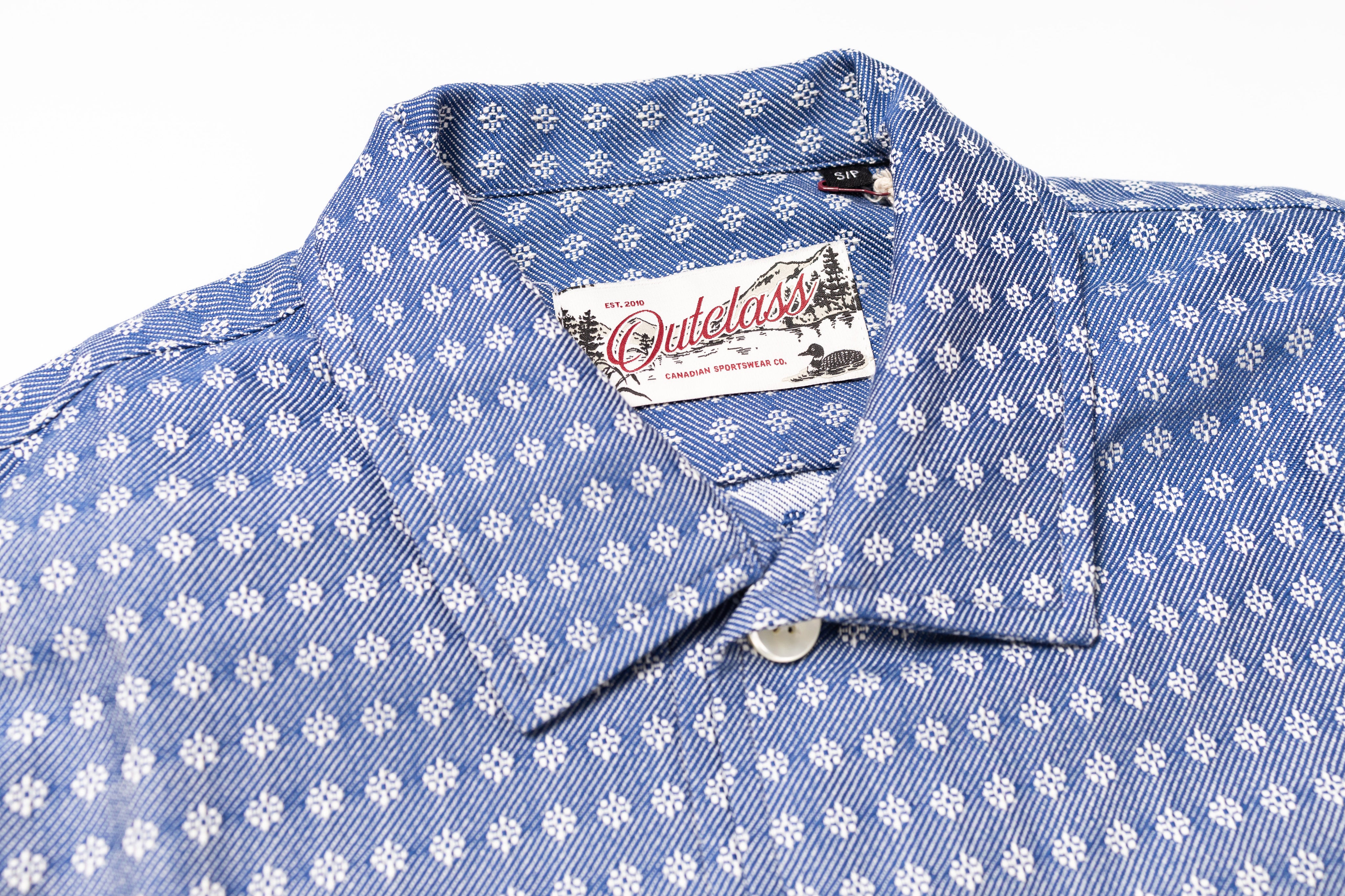 Blue shirt with white floral pattern and Ouletee brand label on a white background