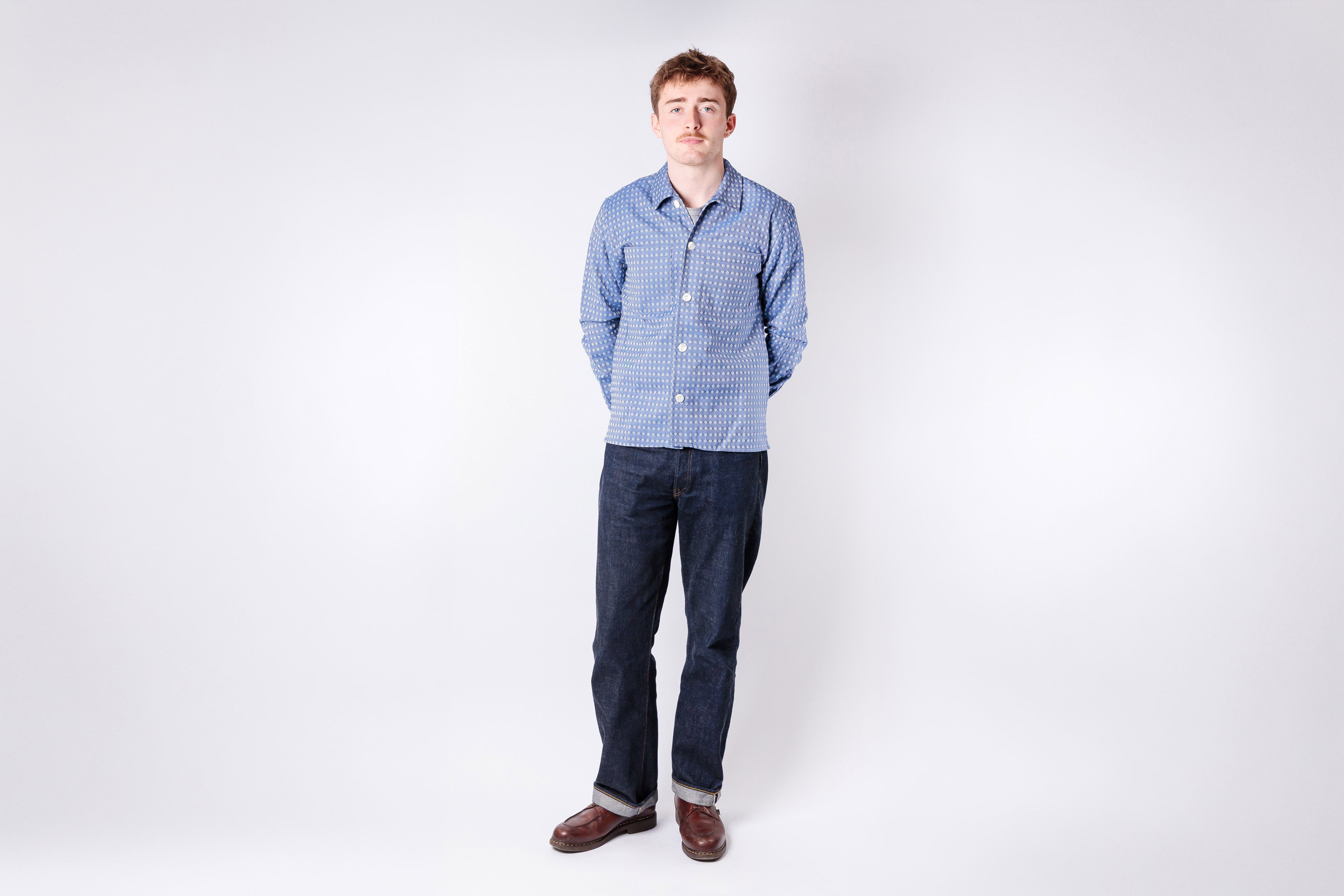 Man wearing a blue checkered shirt and dark jeans standing against a white background