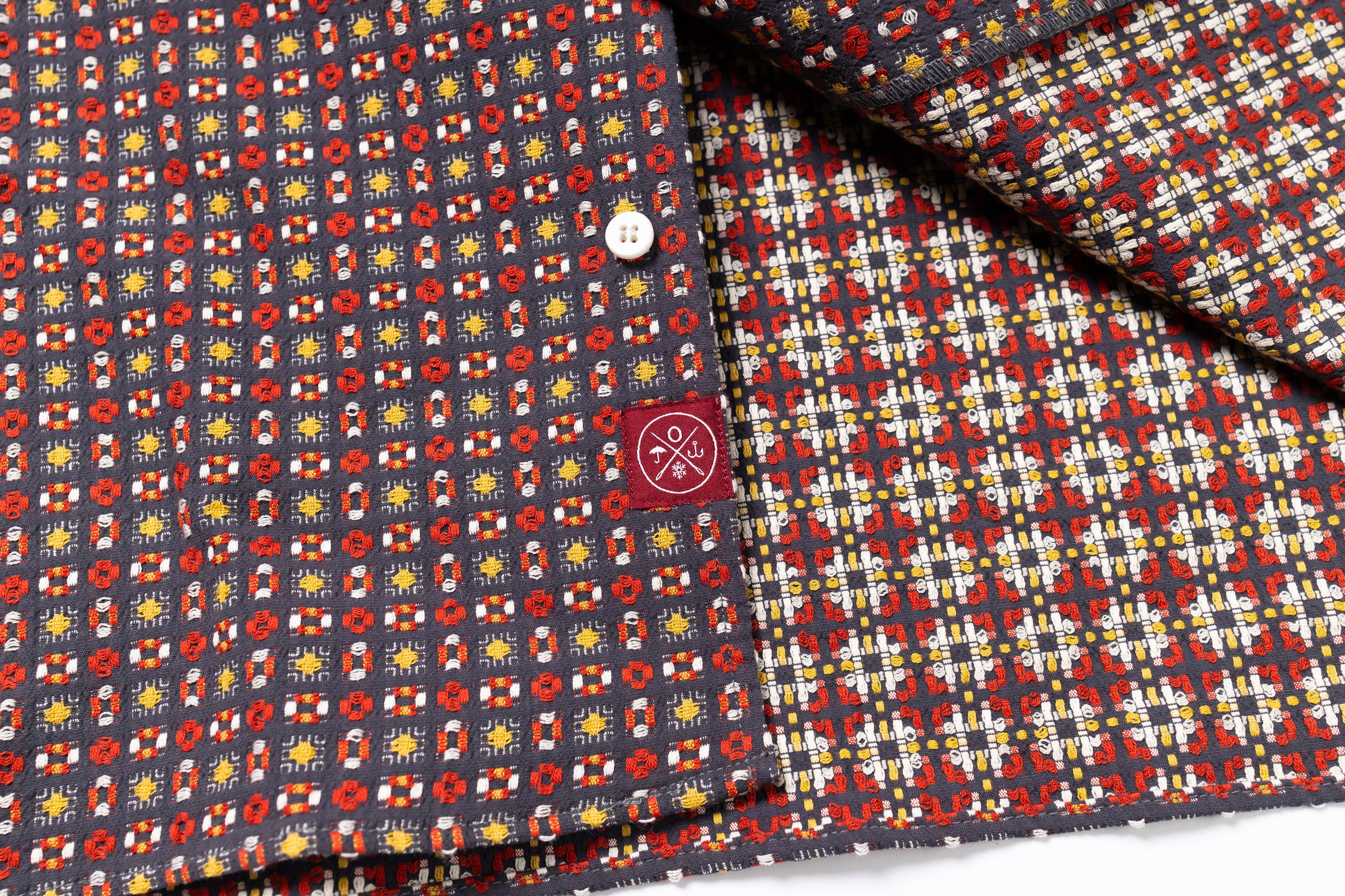 Close-up of patterned fabric with a button and brand logo.