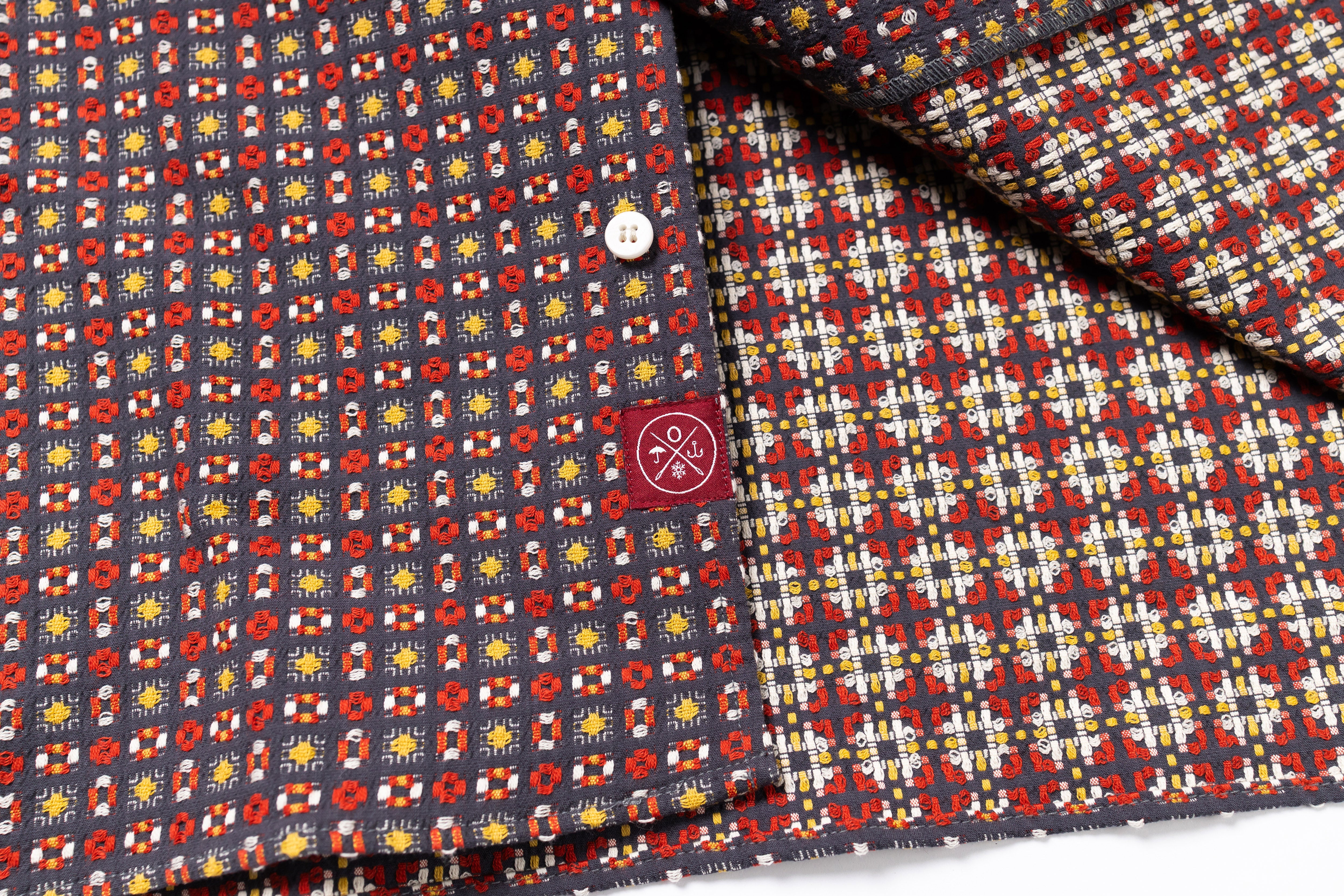 Close-up of patterned fabric with a button and brand logo.