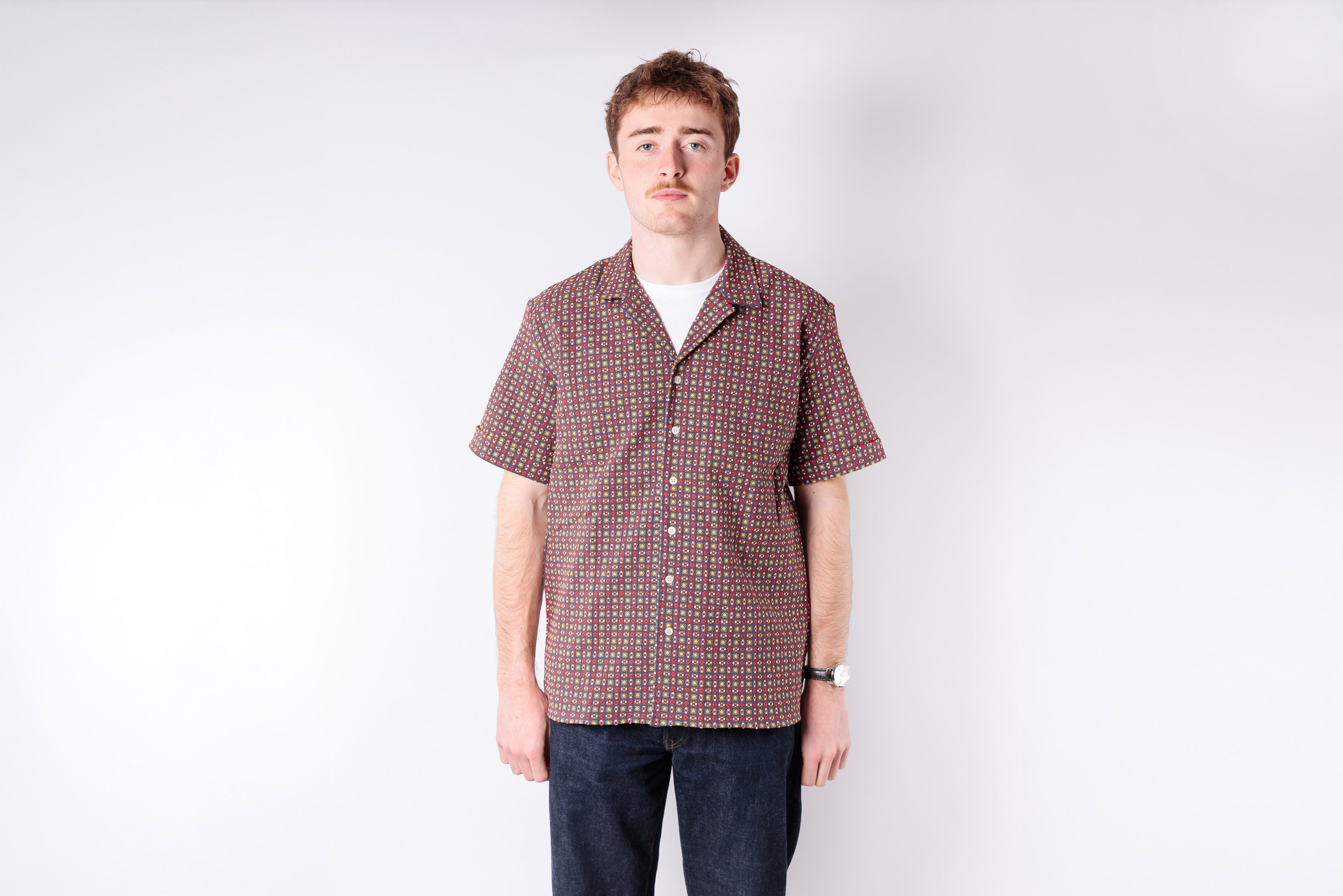 Man wearing a patterned shirt and jeans on a white background