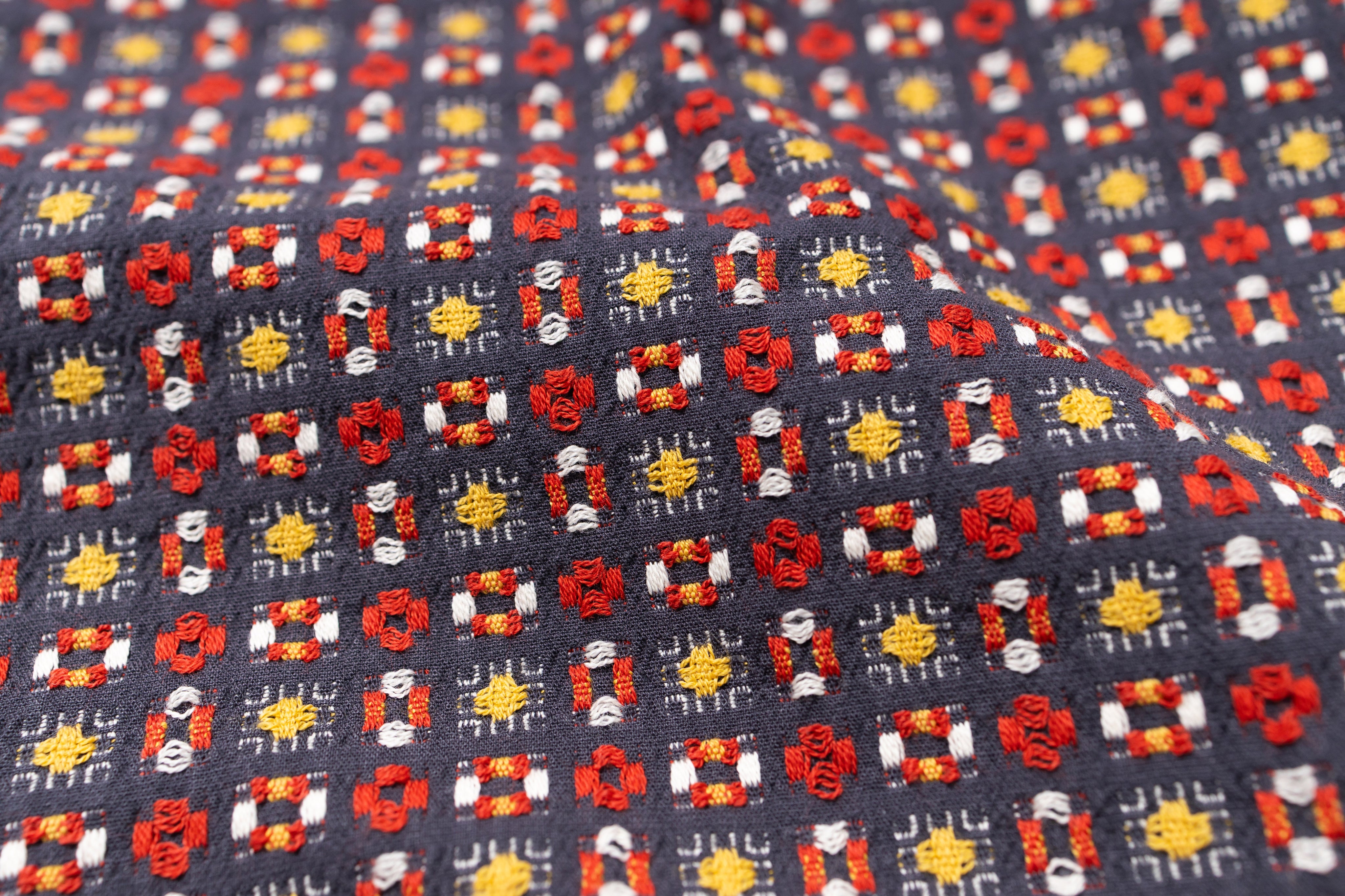 Close-up of patterned fabric with red, yellow, and white designs on a dark background