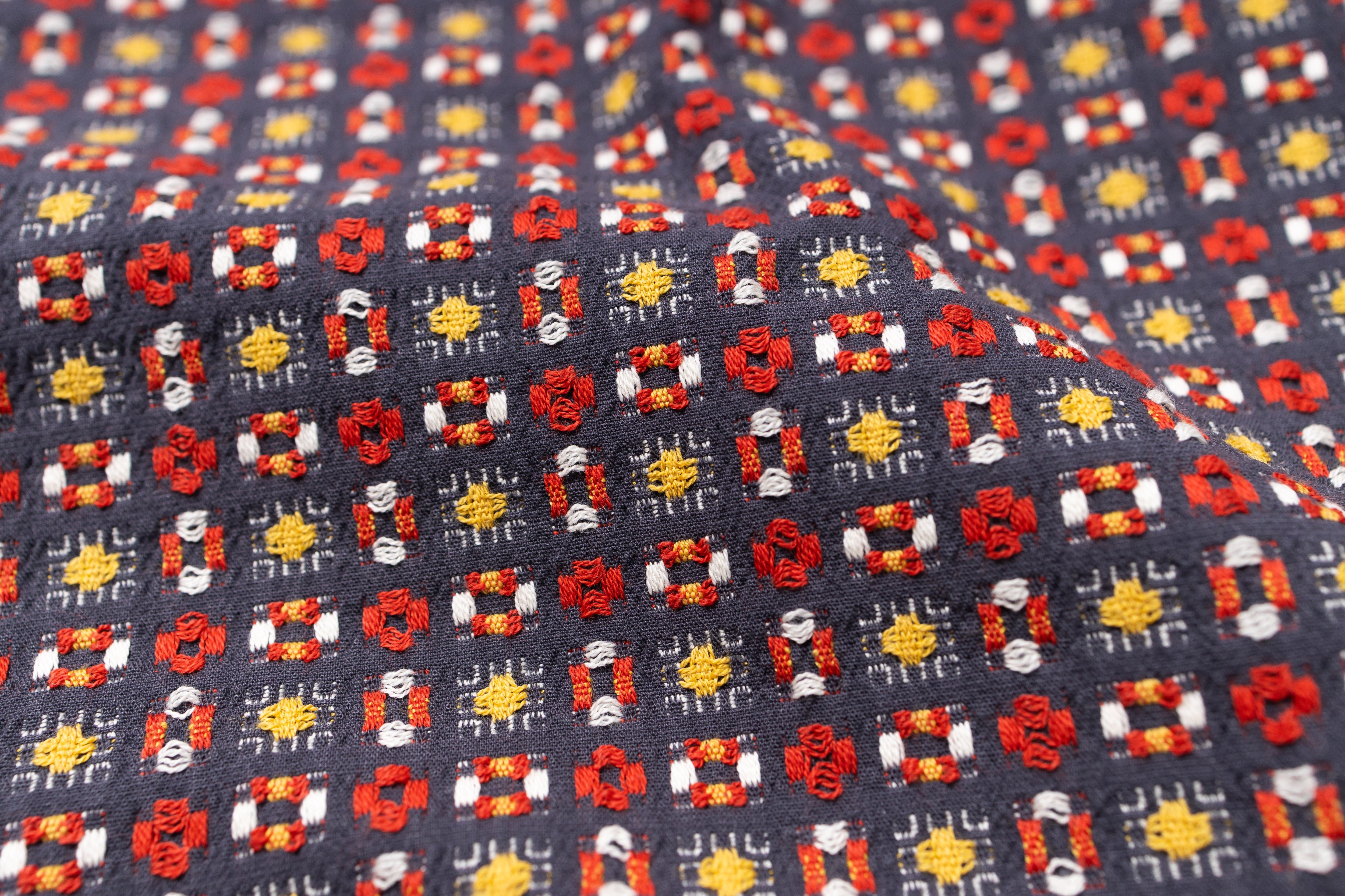Close-up of patterned fabric with red, yellow, and white designs on a dark background