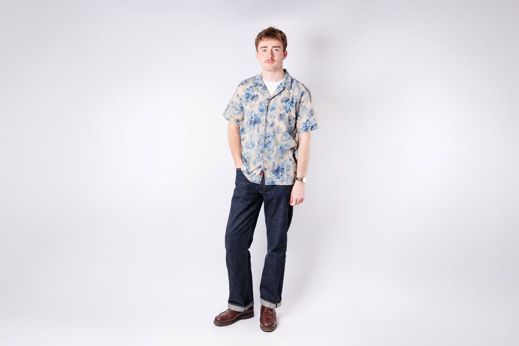 Man wearing a floral shirt and dark pants on a white background