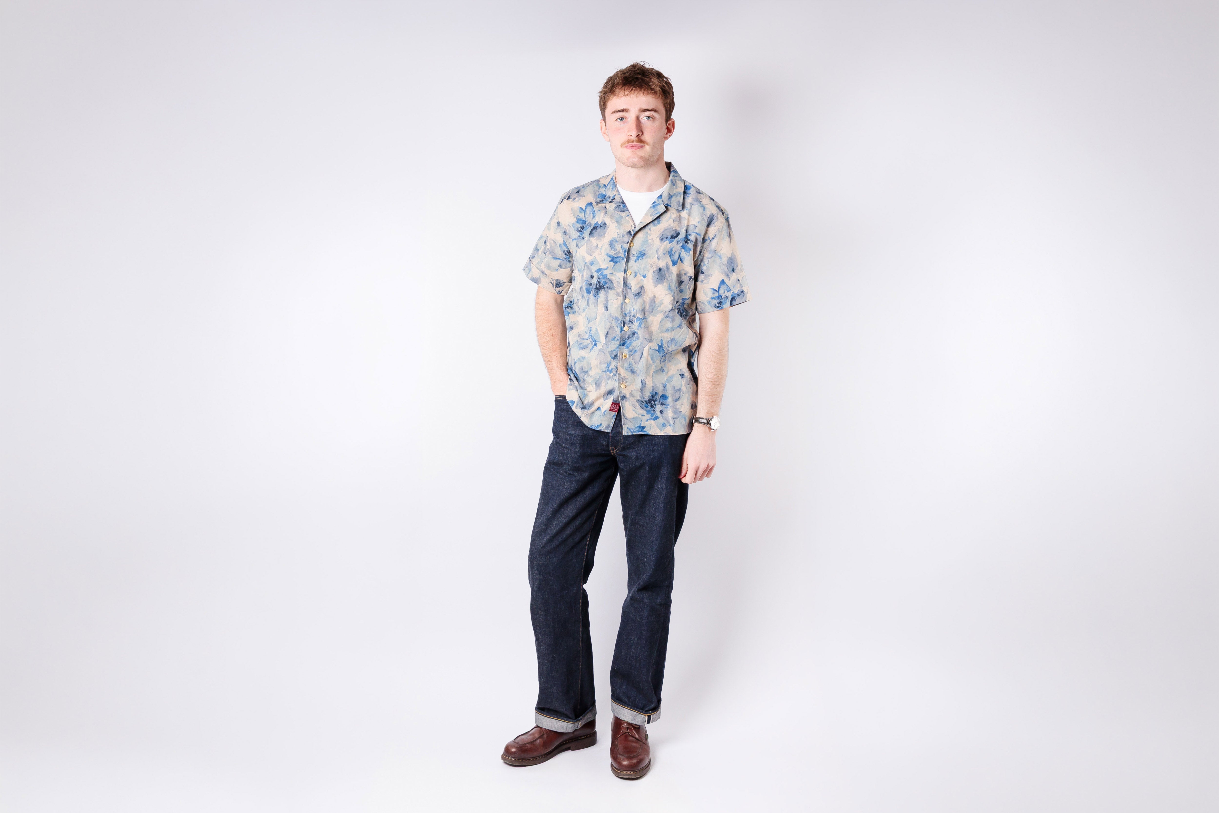 Man wearing a floral shirt and dark pants on a white background