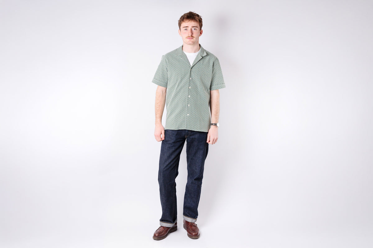 Man wearing a green checkered shirt and dark jeans on a white background