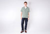 Man wearing a green checkered shirt and dark jeans on a white background