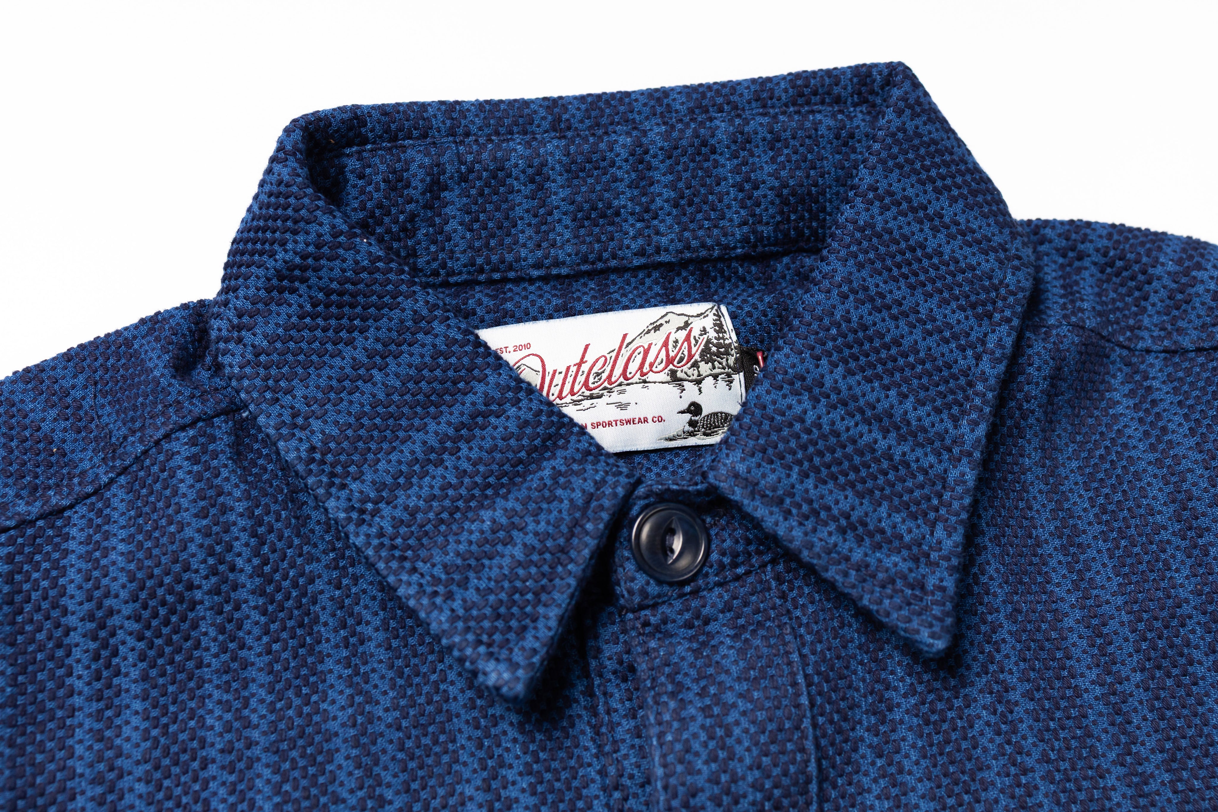 Close-up of a blue textured shirt collar with a brand label on a white background