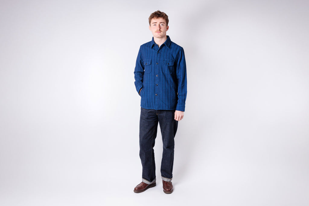 Man wearing a blue shirt and dark pants on a white background